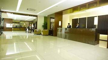 A modern hotel lobby with a reception desk, seating area, and a large plant.