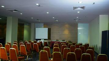 Une salle de conférence avec des rangées de chaises, un écran de projection et une table recouverte d’une nappe.