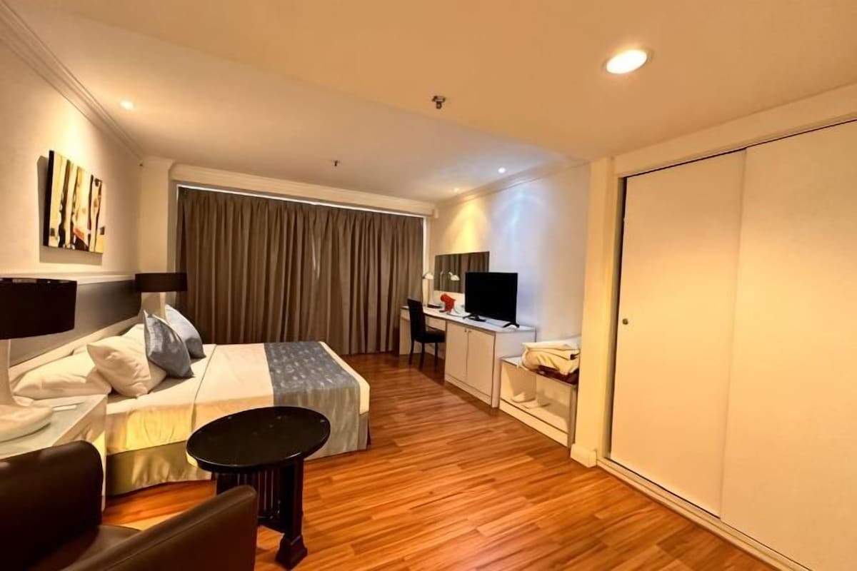 A hotel room with a bed, desk, TV, and wardrobe.
