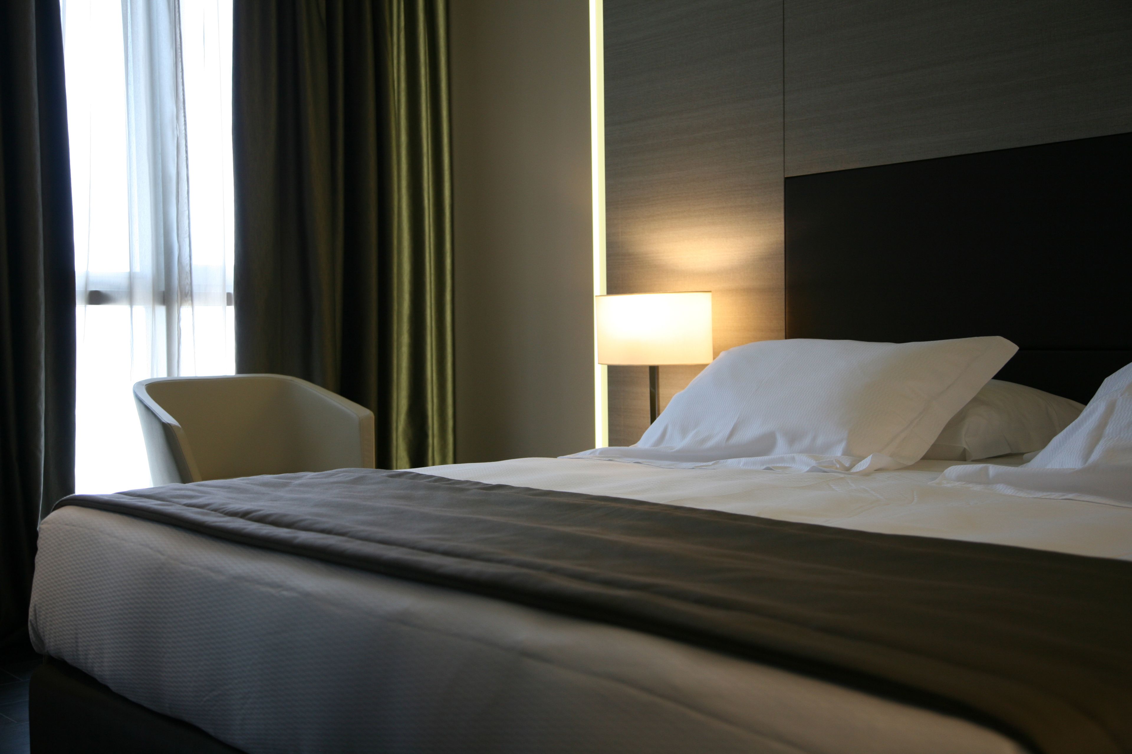 Ett hotellrum med en säng, en stol, en lampa och utsikt över omgivningarna.