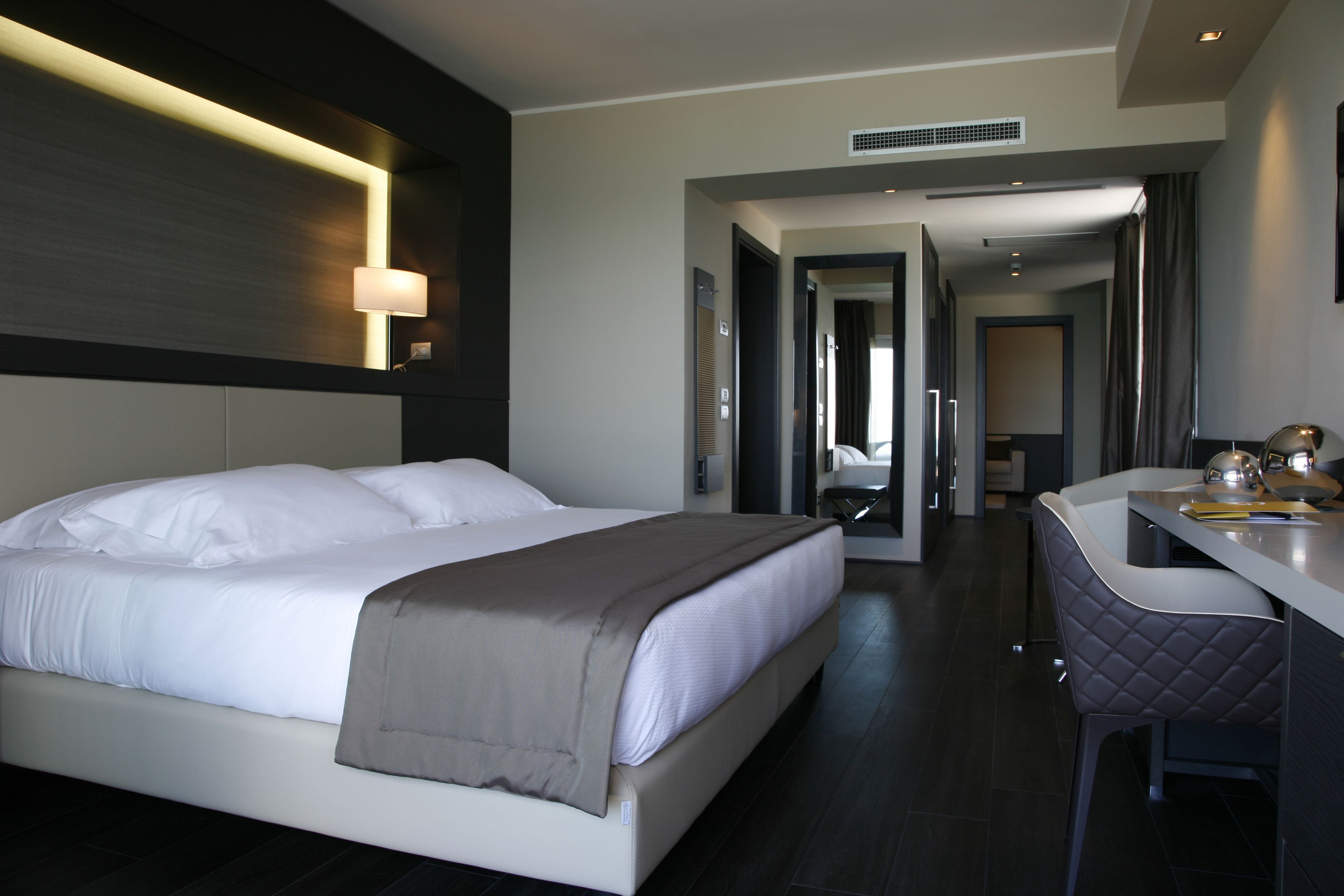 A modern hotel room with a large bed, a desk, and a chair.