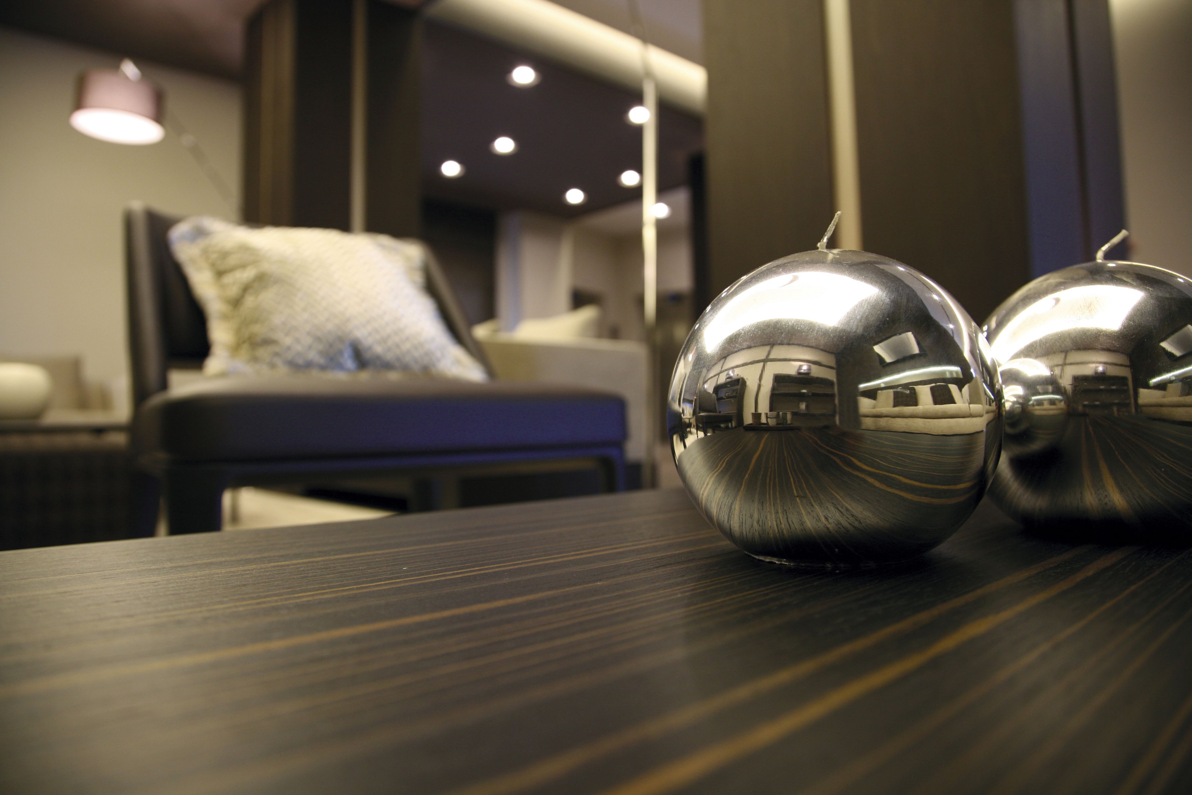 A modern hotel room with a large bed, a bedside table with two spherical objects, and a well-lit room with a lamp.