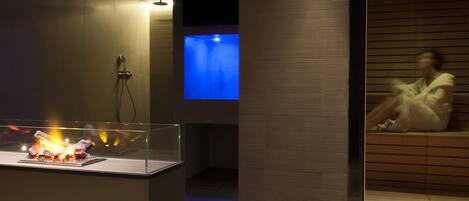 Una moderna sala spa con una panca di legno, un piccolo camino decorativo e una parete illuminata di blu.
