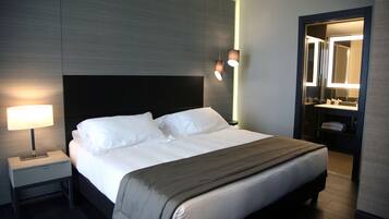 A modern hotel room with a large bed, bedside lamp, and a mirror above the sink.
