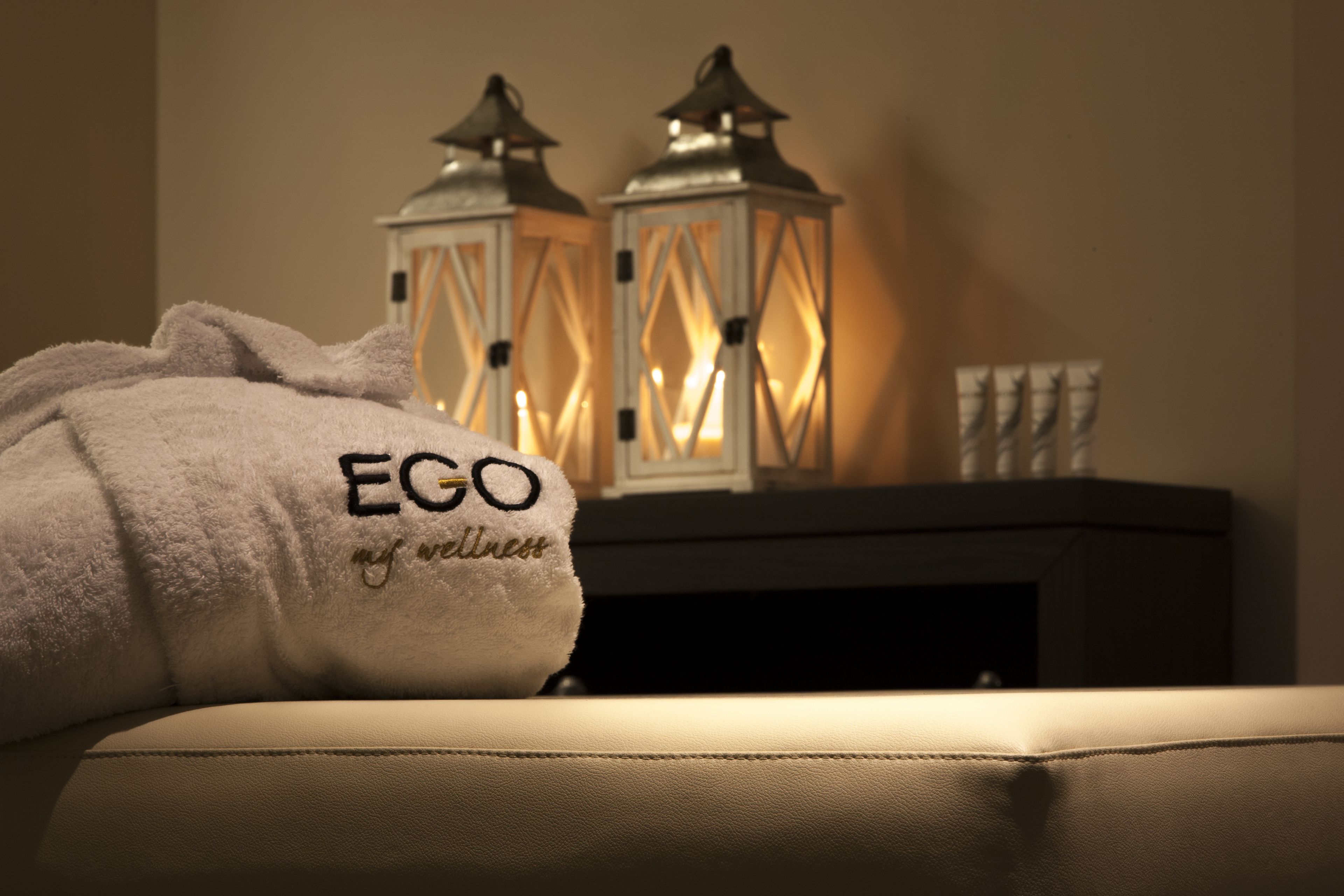 Une serviette blanche avec le texte « EGO my wellness » brodé dessus, posée sur un canapé beige.