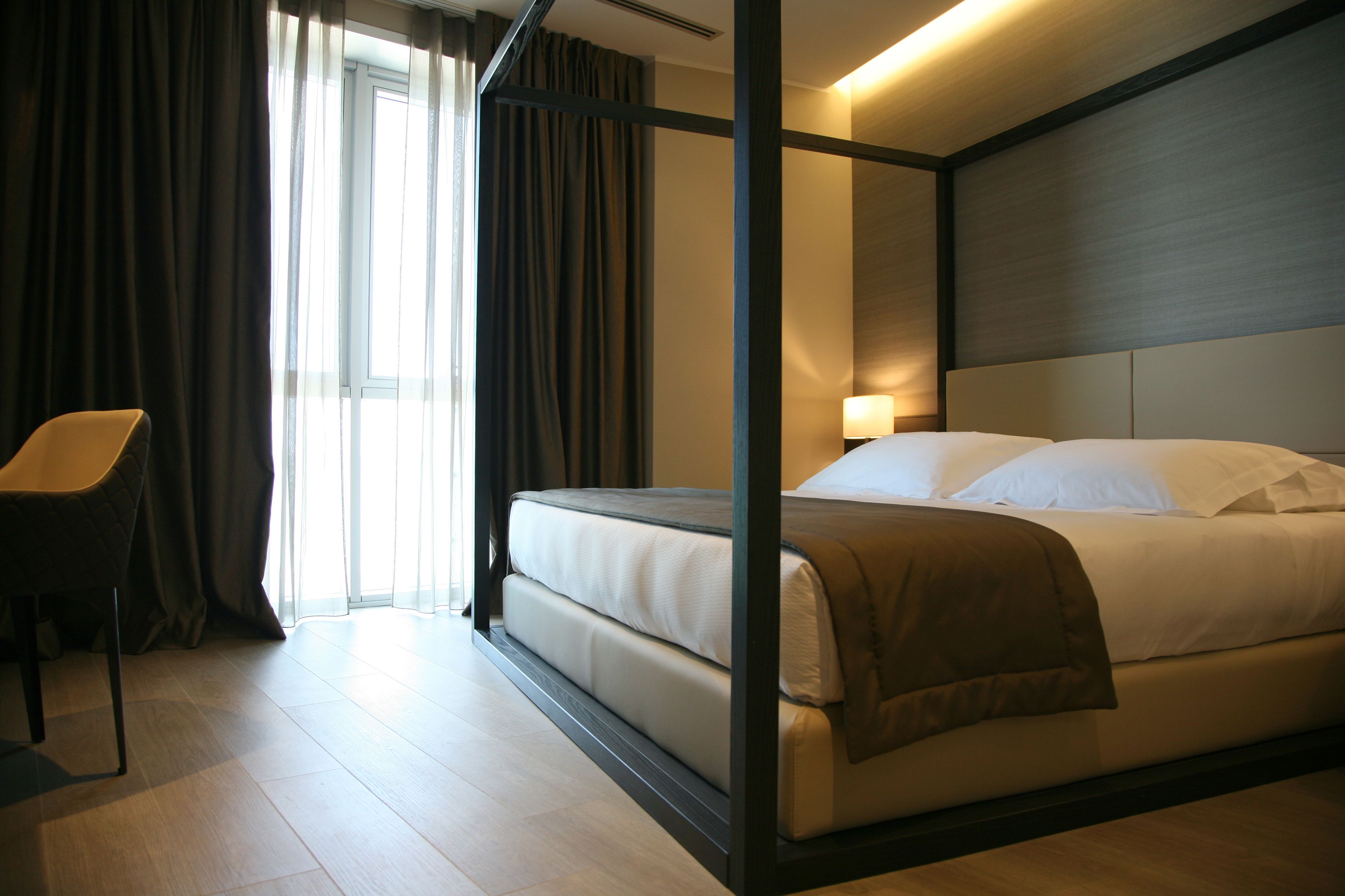 A modern hotel room with a large bed, a chair, and a window with curtains.