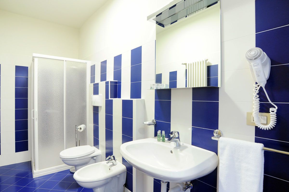 Une salle de bain avec une douche, deux toilettes, un lavabo et un sèche-cheveux fixé au mur.