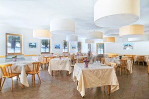 Un restaurante con varias mesas cubiertas con manteles blancos, sillas de madera y lámparas colgantes grandes.