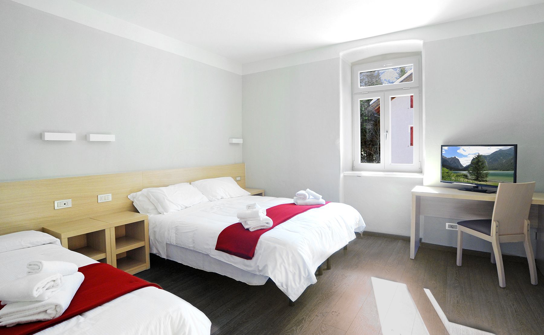 Une chambre d’hôtel avec deux lits, un bureau avec un ordinateur, une fenêtre donnant sur la montagne et une télévision.