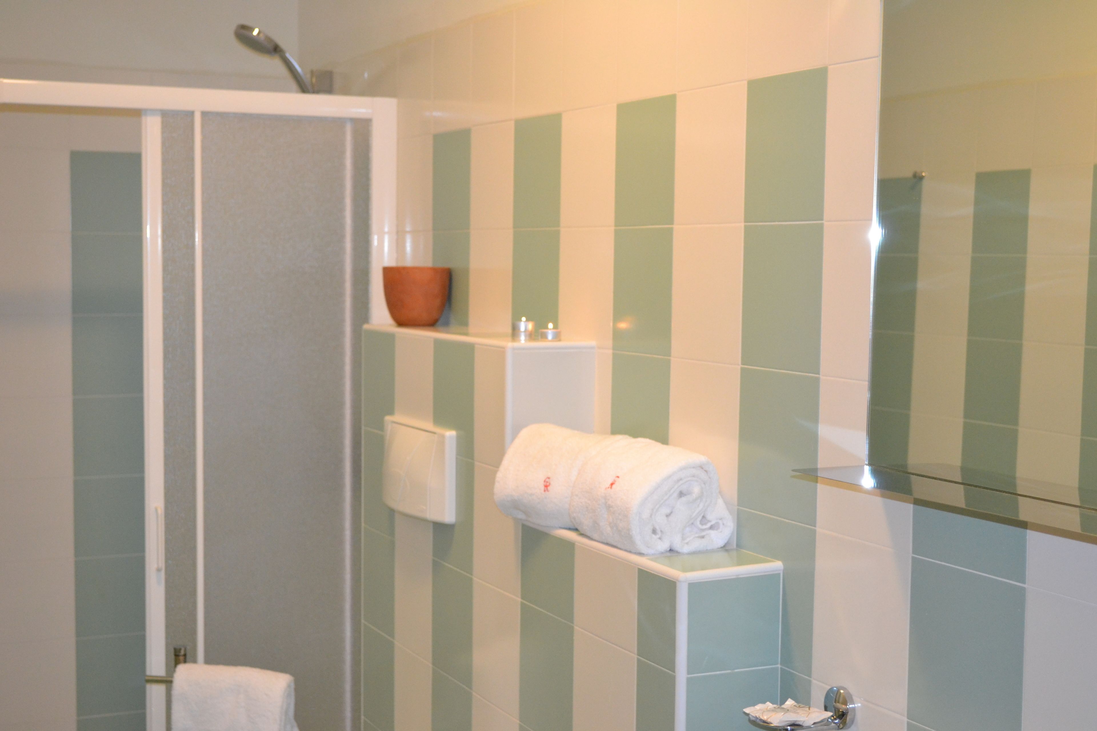 Un baño con azulejos verdes y blancos, ducha, toallero y jabonera.