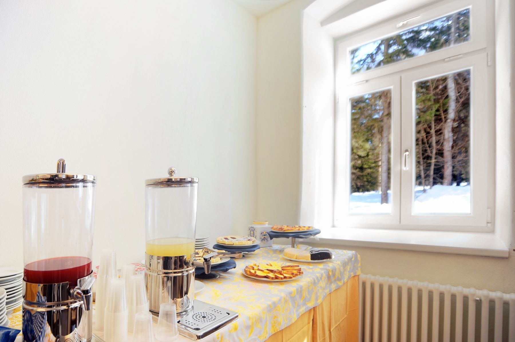 Preparación para el desayuno con una cafetera, un dispensador de jugo y una mesa de buffet con diferentes opciones de comida.