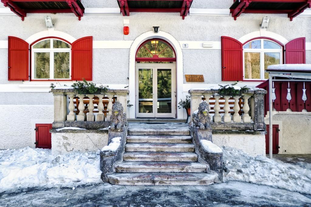 A building with a red door, white walls, and red shutters. There are steps leading to the door, and a small red door to the left.