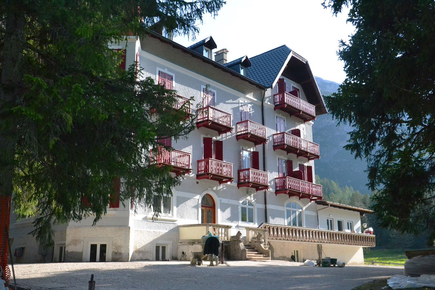 A multi-story building with red balconies, a stone facade, and a mountainous backdrop.