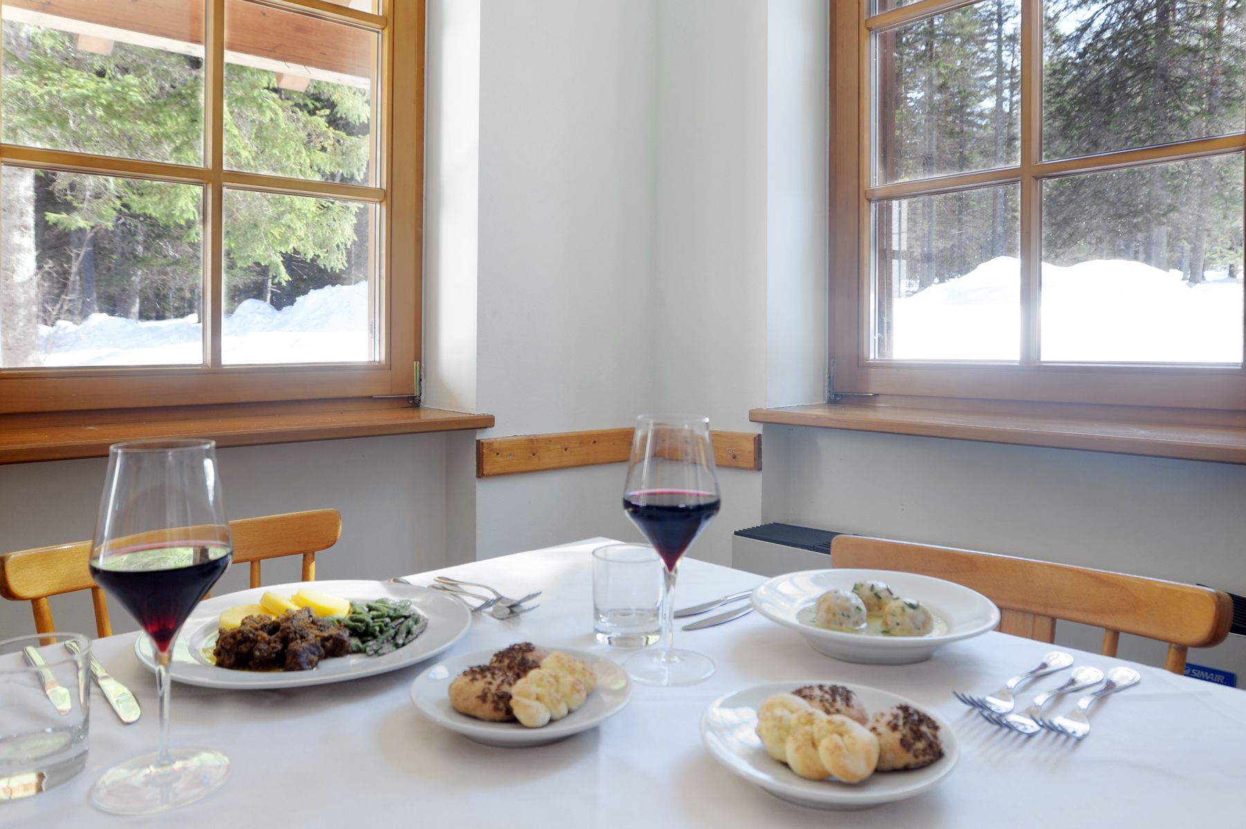 A dining table with plates of food, wine glasses, and cutlery.