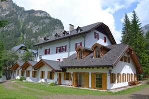 Un edificio de estilo chalé con varias ventanas y techo inclinado, rodeado de un paisaje montañoso.