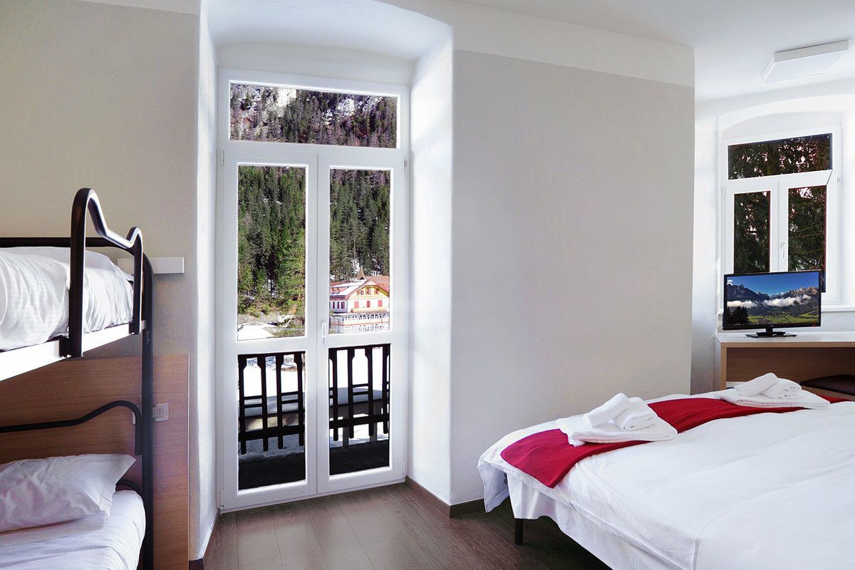 Una camera d'albergo con un letto, una scrivania con un computer e una finestra vista alberi ed edifici.