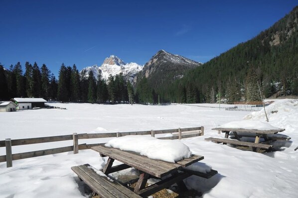 A snowy outdoor area with wooden picnic tables and a mountain in the background. - Hotel Croda Rossa (Dobbiaco)