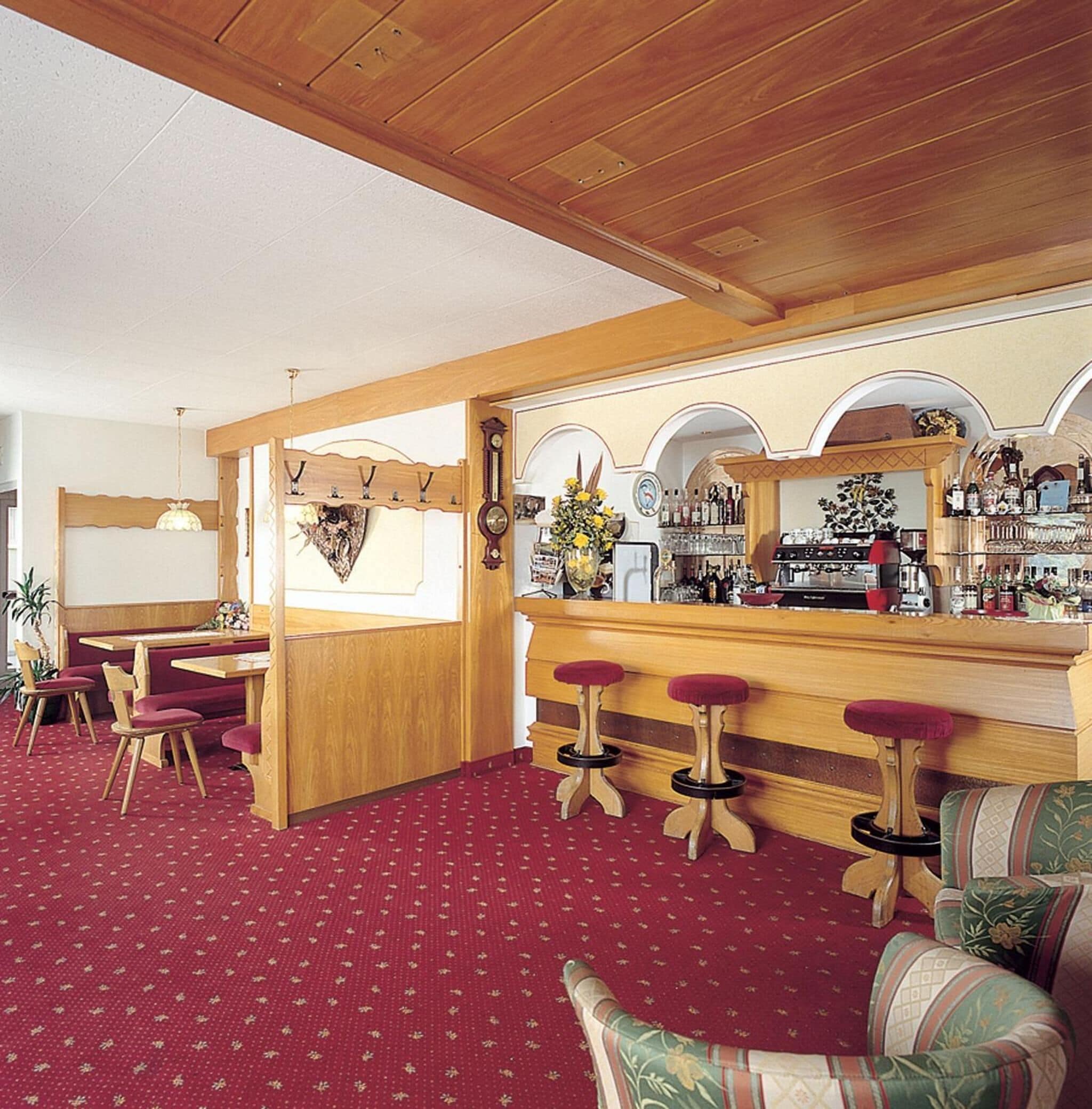 A cozy bar area with wooden stools, a bar counter, and a dining area with a booth and chairs.