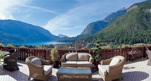 A terrace with wicker furniture, a view of a lake, and mountains in the background. - Hotel Olympia (Molveno)