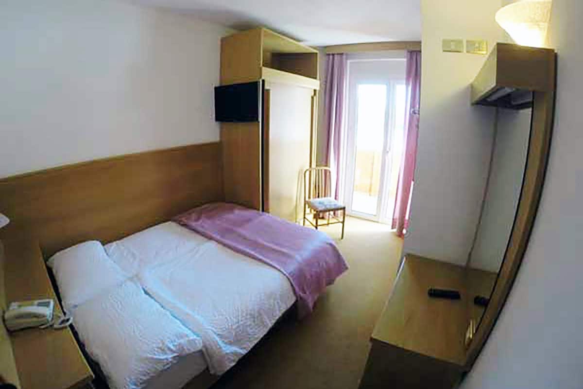 Una habitación de hotel con cama, una silla, un escritorio, una lámpara y un televisor.