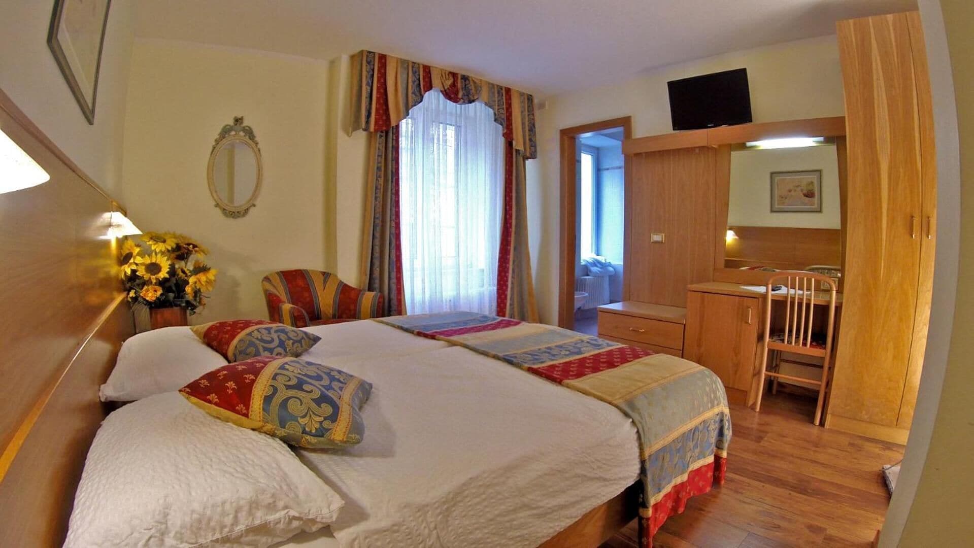 Une chambre d’hôtel avec un grand lit, un bureau, une chaise, une télévision et une fenêtre avec des rideaux.