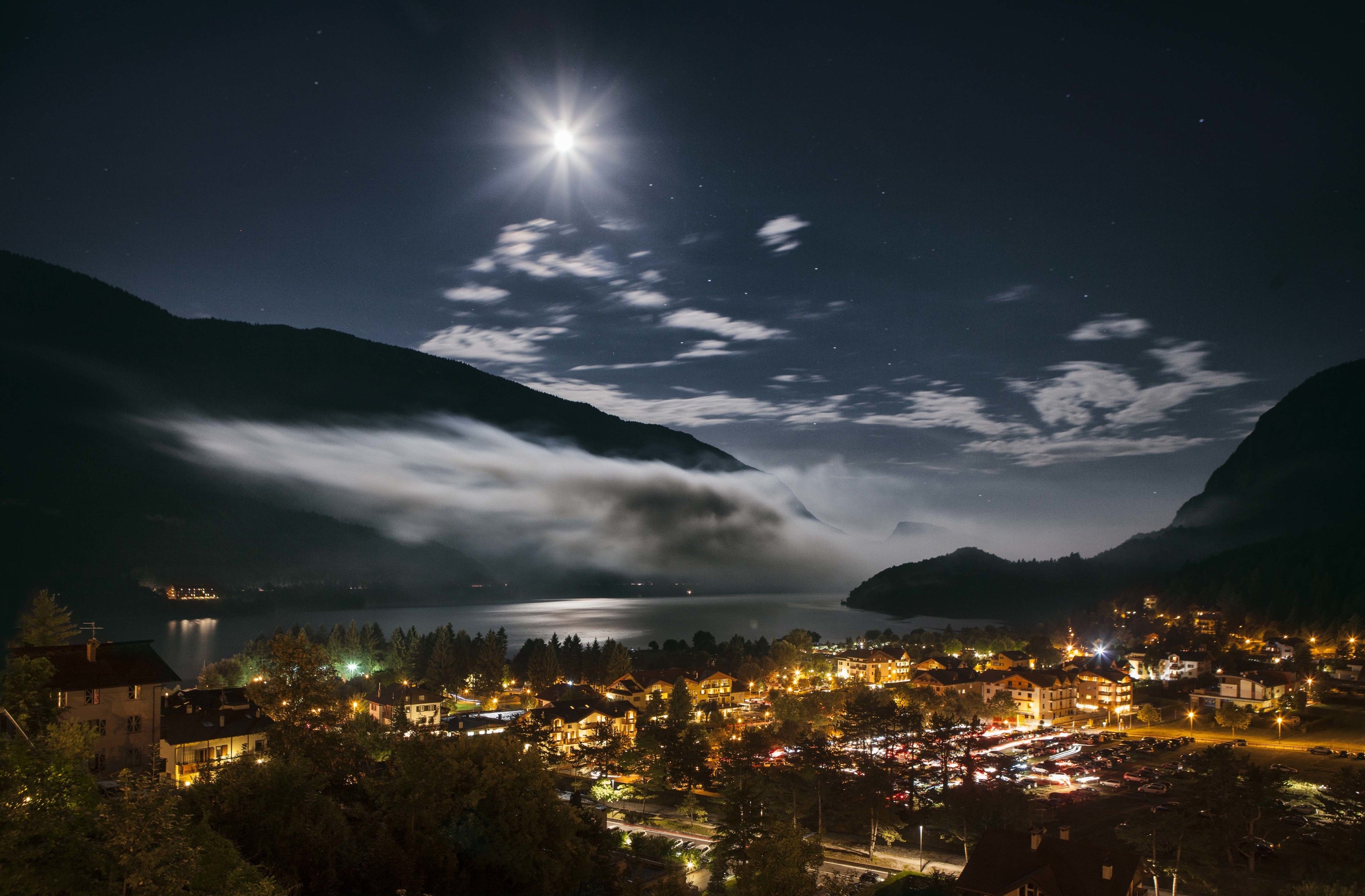 A nighttime view of a town by a lake with mountains in the background.