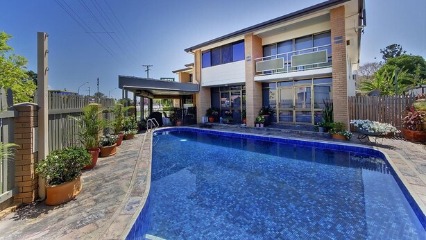 A modern two-story hotel with a swimming pool, potted plants, and a fenced backyard. - Raintree Motel (Hermit Park)