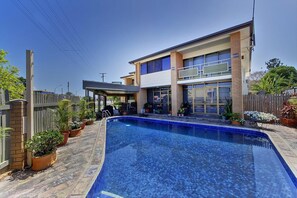 A modern two-story hotel with a swimming pool, potted plants, and a fenced backyard.