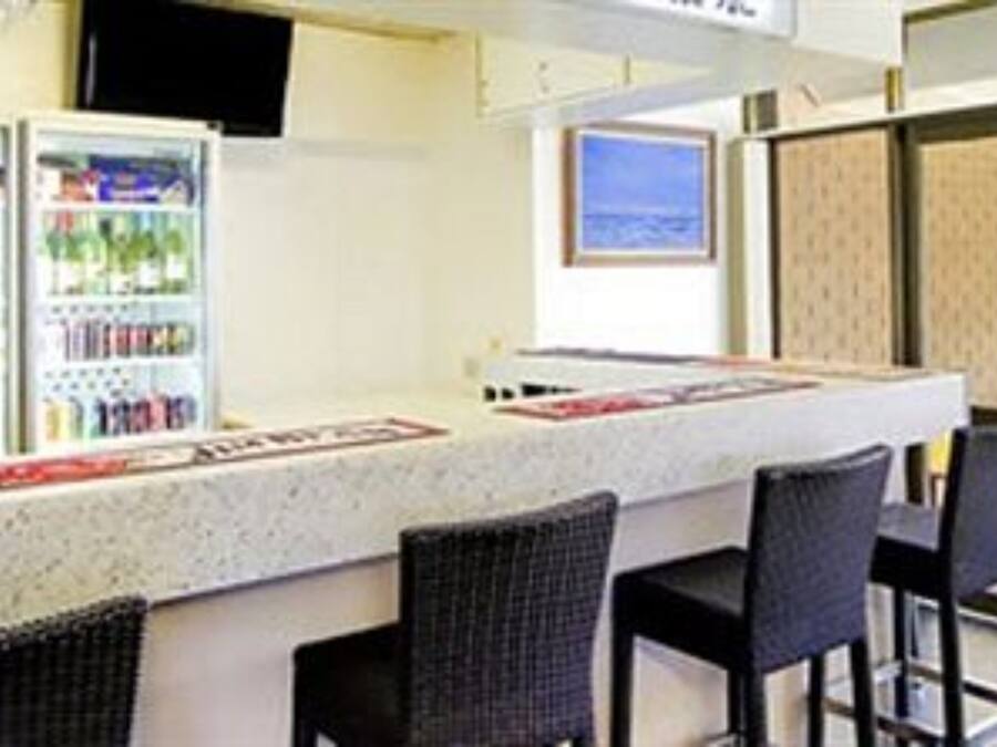 Una zona de bar con mostrador, asientos y un refrigerador lleno de bebidas.