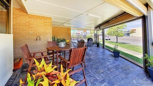 A covered patio with a brick wall, a wooden table and chairs, and a fire pit. - Raintree Motel (Hermit Park)