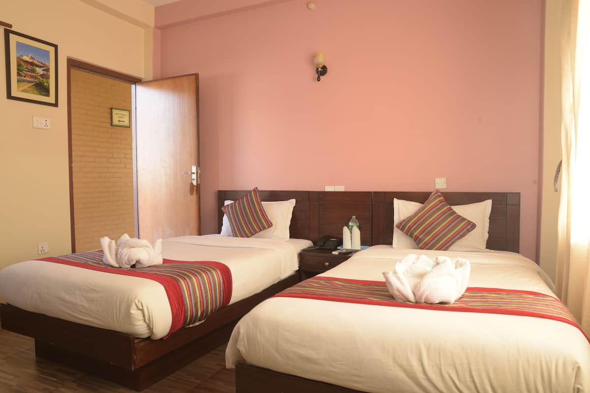 A hotel room with two beds, each with a striped blanket and a towel. There is a nightstand with a phone and a bottle. The room has a wooden headboard and a pink wall.