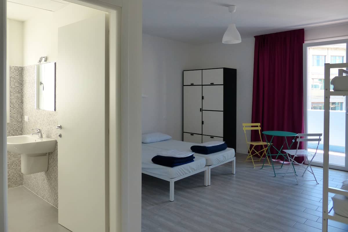 Quarto com duas camas, um guarda-roupa, uma mesinha e uma cadeira.