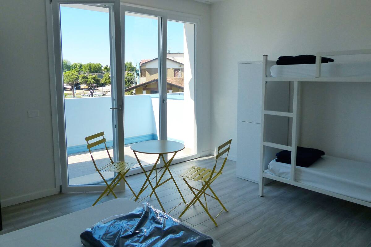 Quarto com varanda, sofá branco, mesa pequena e duas cadeiras amarelas.
