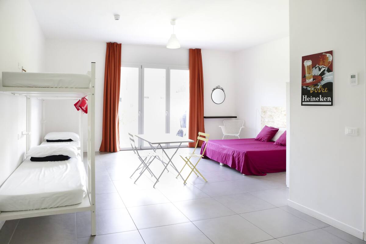 Quarto com beliches, uma mesa de jantar e uma cama com colcha roxa.