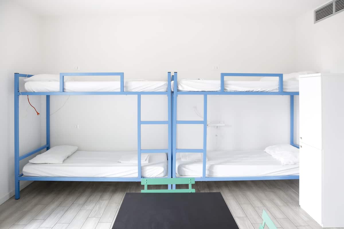 Quarto com beliche, parede branca, tapete preto no pé da cama e guarda-roupa branco à direita.