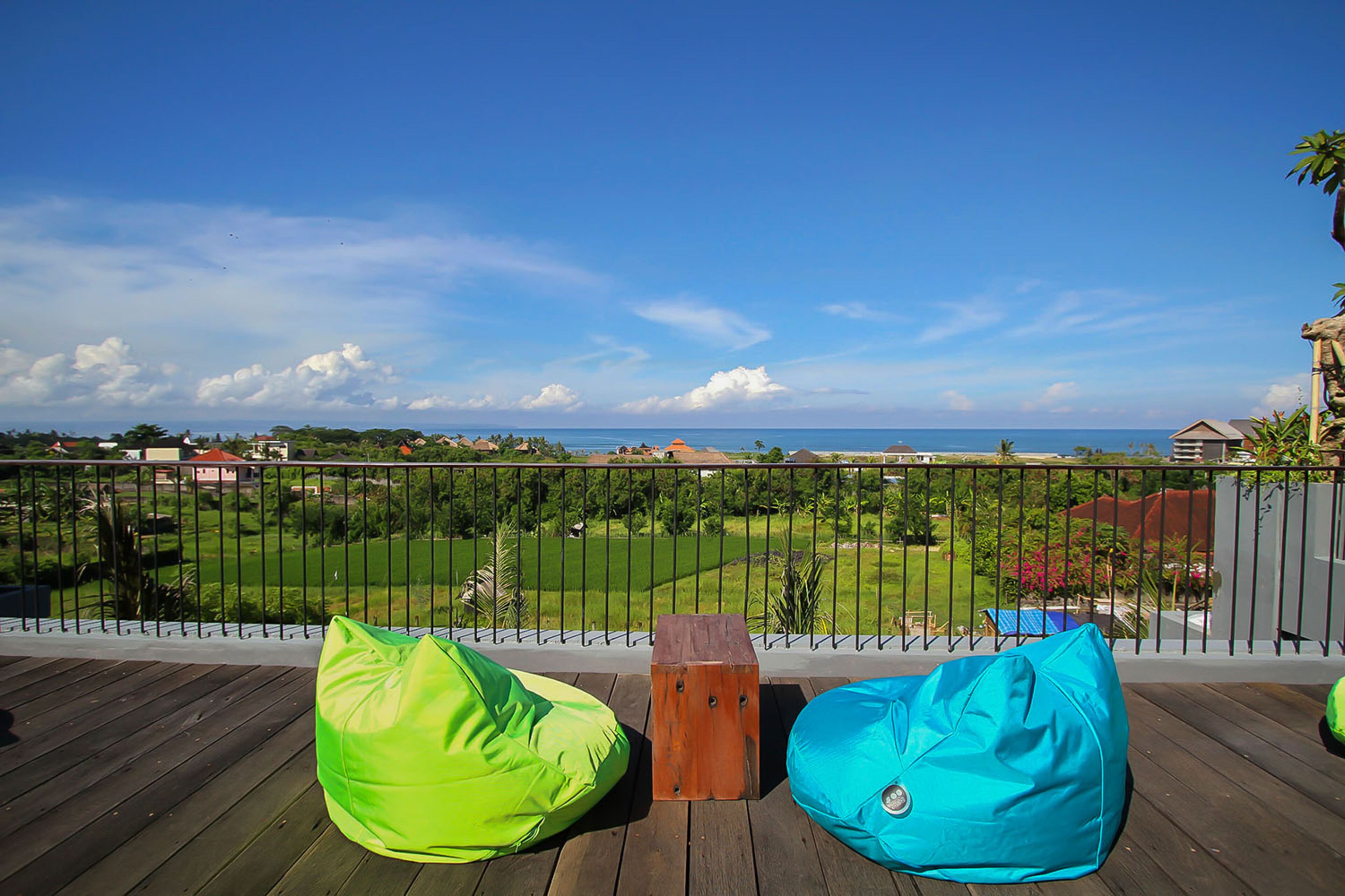 A balcony with two bean bags and a wooden stool, overlooking a grassy area and the ocean.