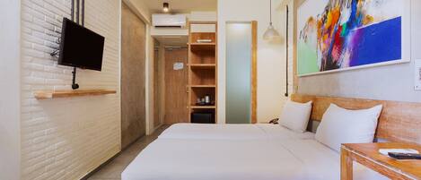Quarto de hotel com cama, televisão na parede, um quadro e mesa de madeira.