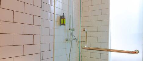 A bathroom with a glass shower enclosure, white tiled walls, a white toilet, and a glass door with a frosted window.