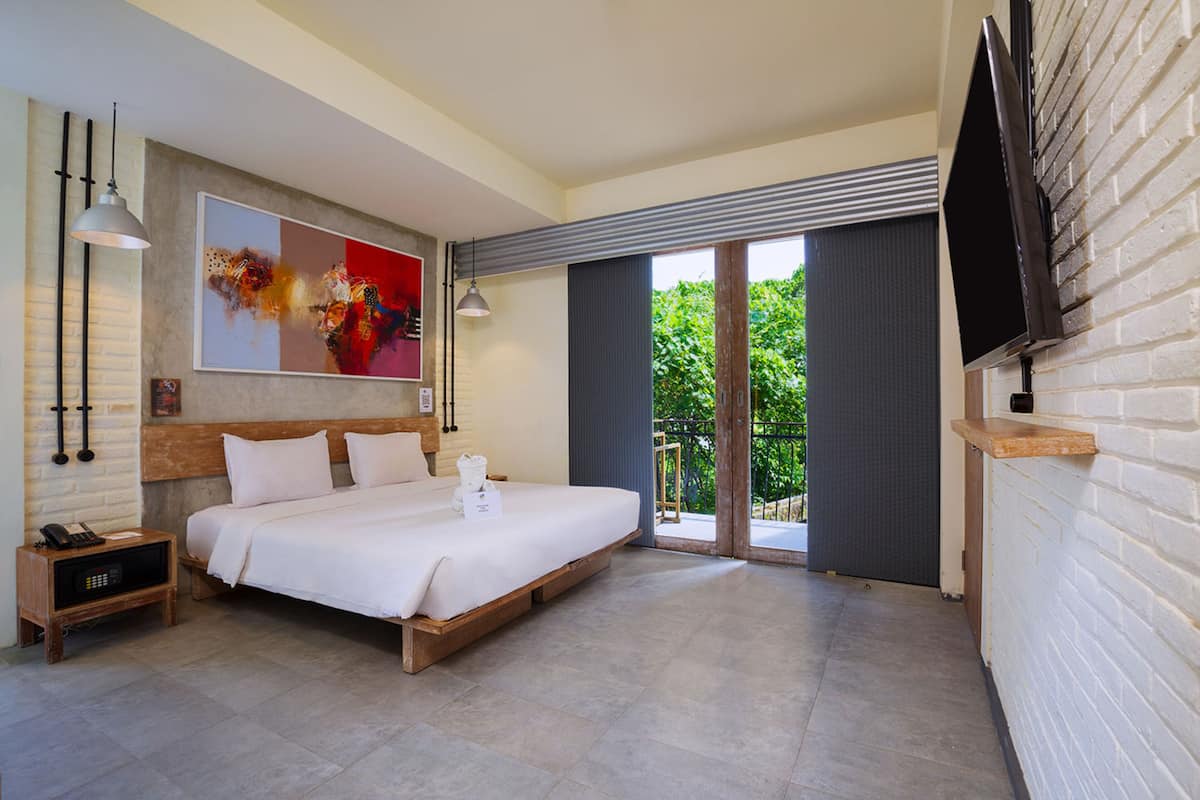 Una habitación de hotel moderna con una cama grande, un televisor de pantalla plana montado en la pared y un ventanal corredero que da a un balcón.