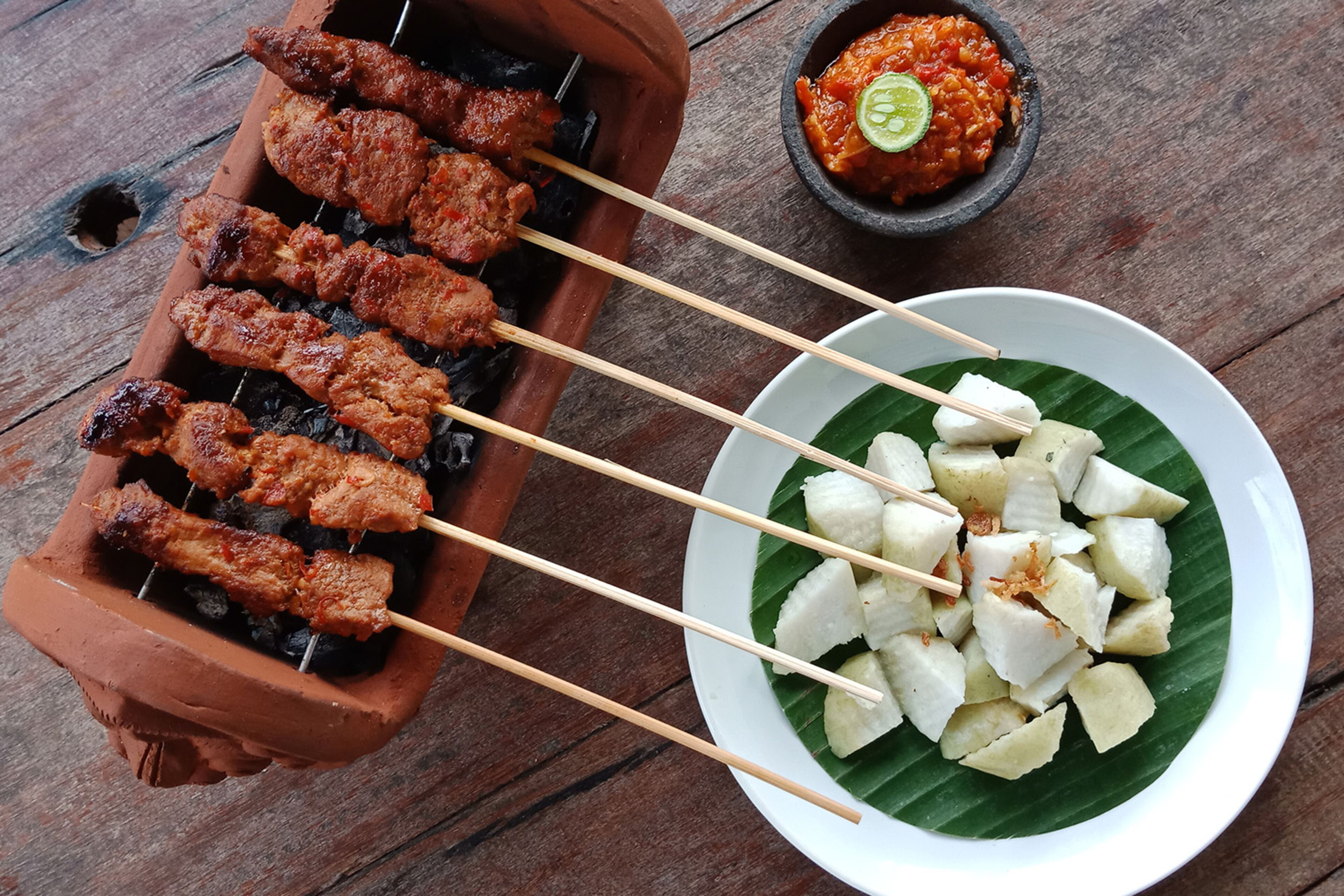 Skewers of grilled meat and a bowl of diced fruit on a plate.