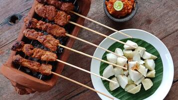 Skewers of grilled meat and a bowl of diced fruit on a plate.