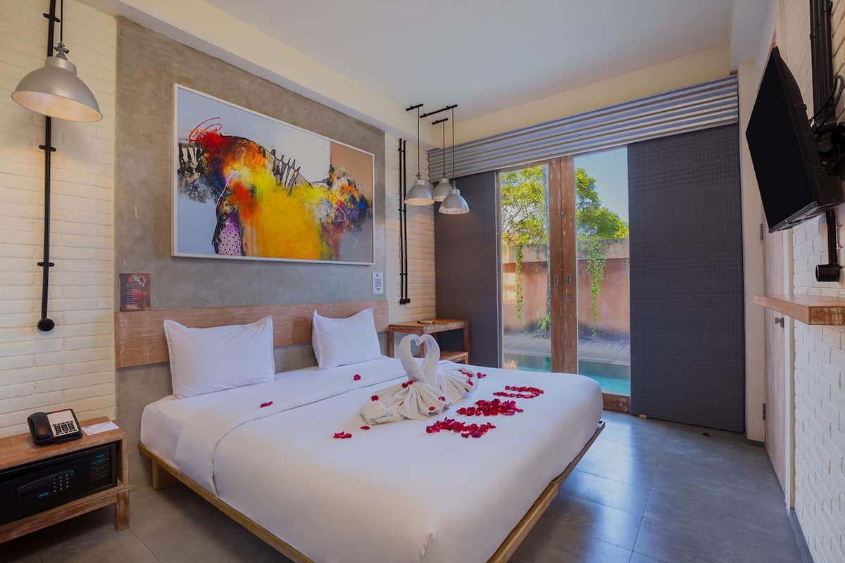Una habitación de hotel con una cama grande, un cuadro en la pared, un teléfono en la mesita de noche y un televisor montado.