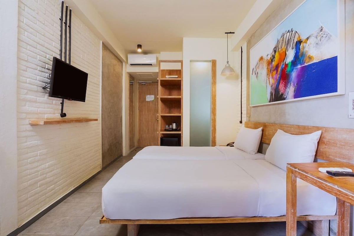 Een hotelkamer met een bed, een aan de muur bevestigde televisie, een schilderij en een houten tafel.