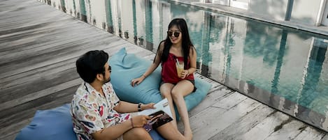 Two people sitting on a blue bean bag chair by a poolside.