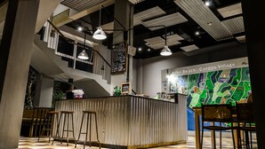 A modern bar area with high ceilings, exposed beams, and a checkered floor. There are bar stools, a counter, and a map on the wall. - FRii Bali Echo Beach (Canggu)