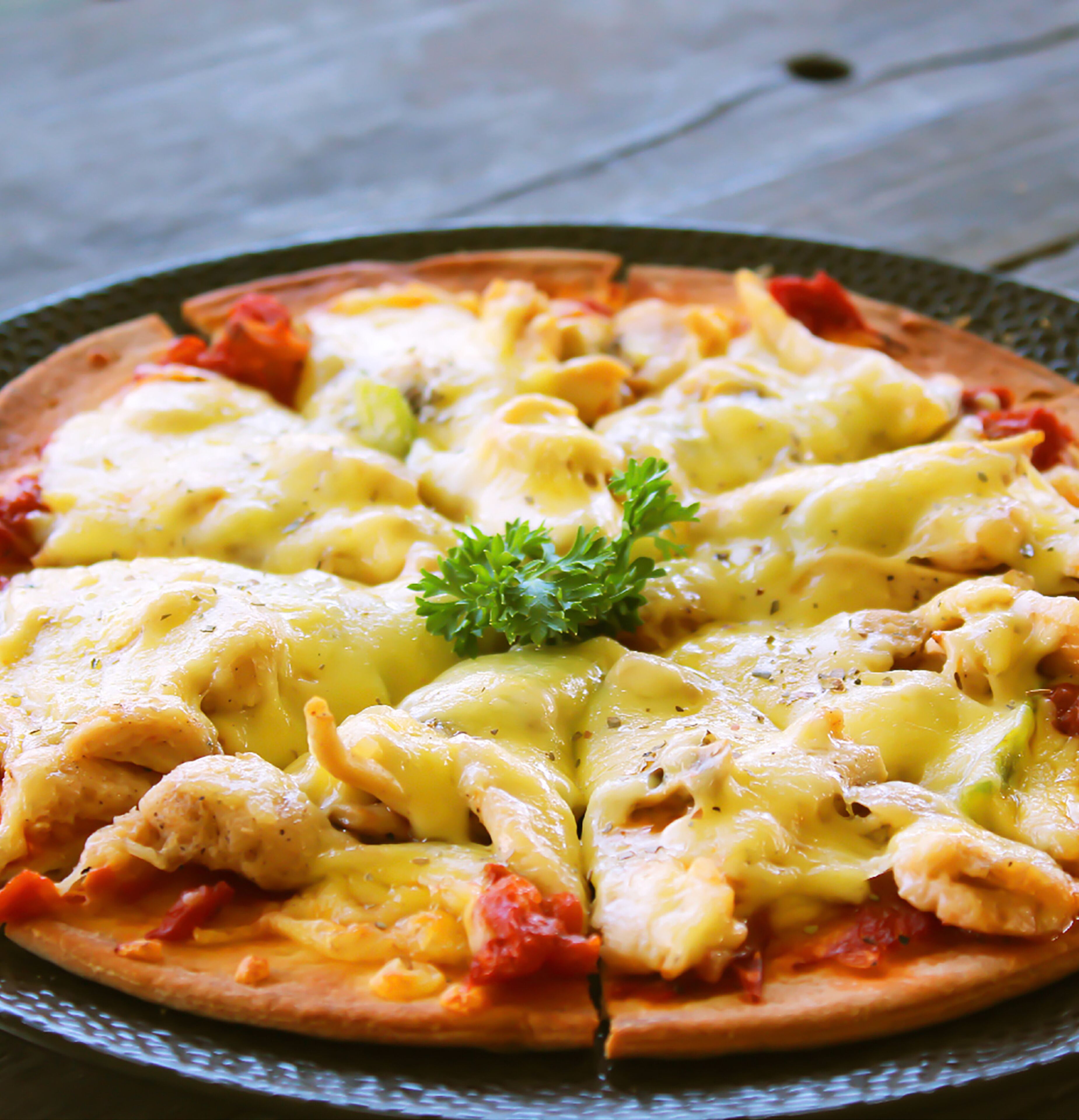 A pizza with cheese and tomato sauce, garnished with parsley, on a round plate.