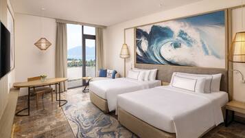 Habitación de hotel con dos camas, una mesa de comedor, un televisor y un cuadro de un amplio panorama marino.