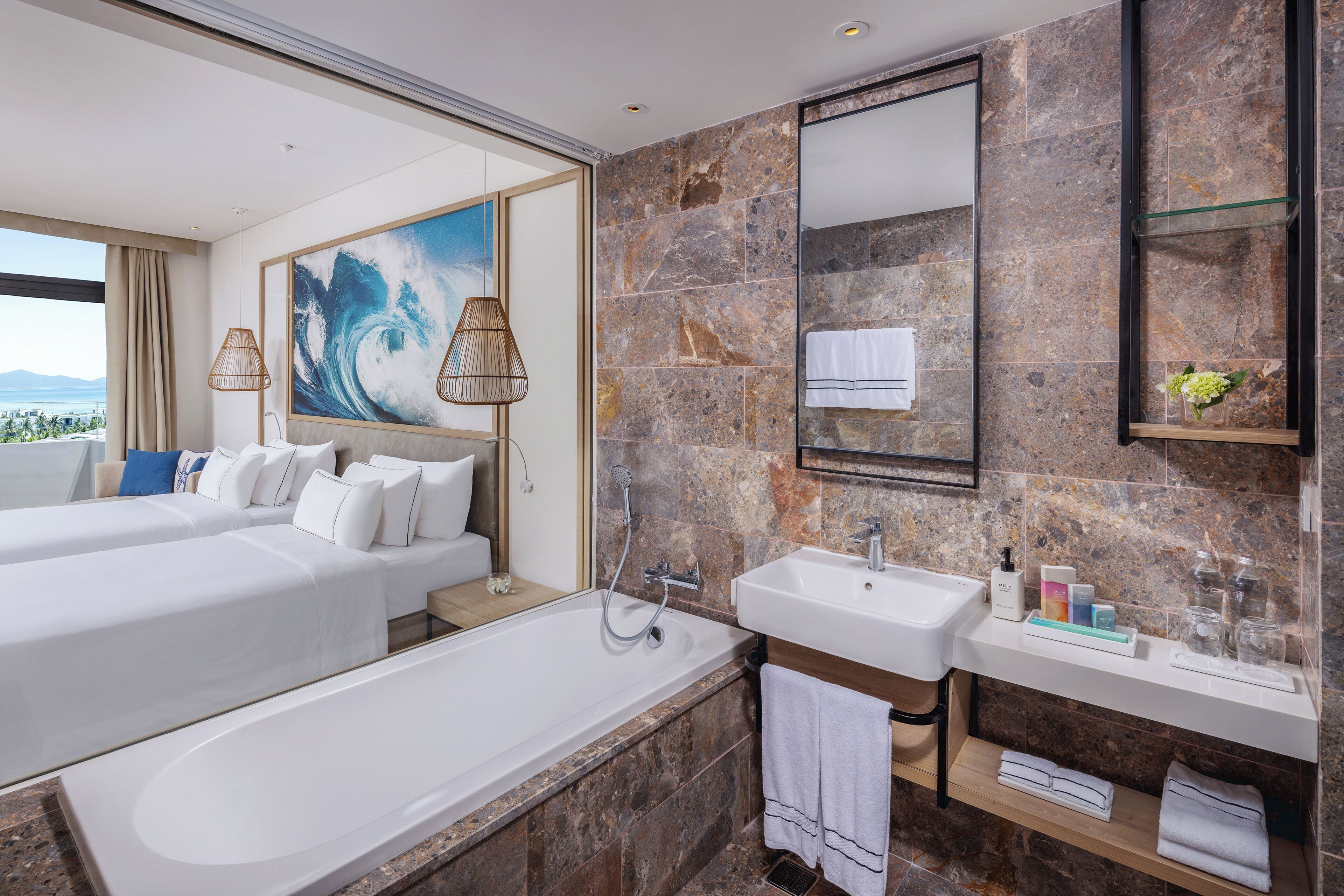 A modern hotel bathroom with a large bathtub, two white beds, a large mirror, and a view of the city.