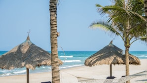 A beach scene with thatched umbrellas, lounge chairs, and a hammock.