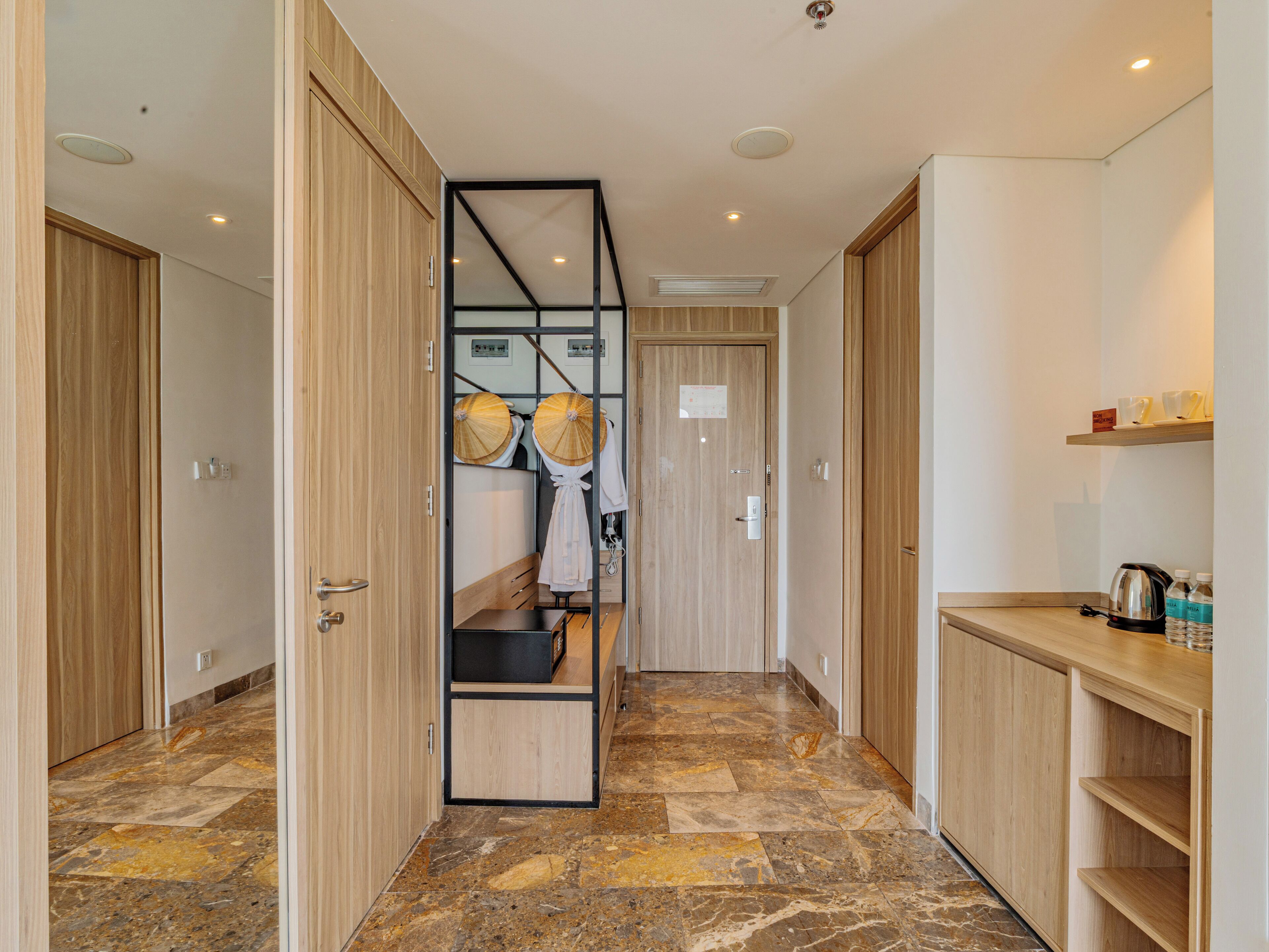 A modern hotel corridor with wooden doors, a stone-tiled floor, and a kitchenette area with a kettle and cups.